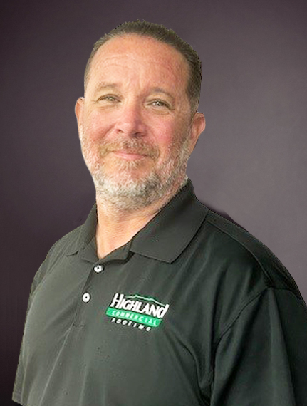 A man with short hair and a beard is wearing a black shirt with the logo "Highland Roofing" on it. He is smiling slightly and standing against a dark background.