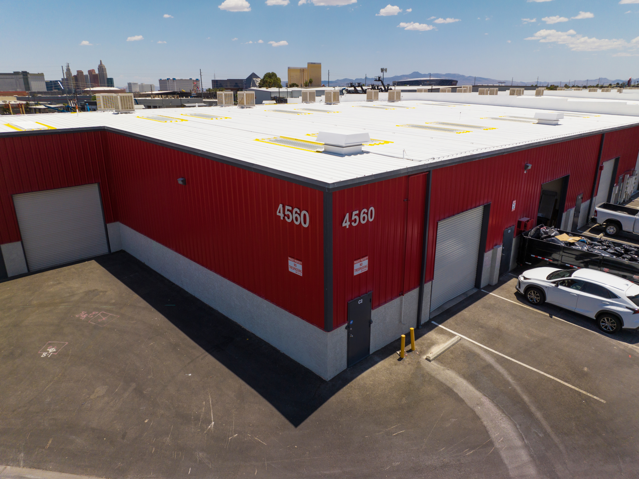 A large red industrial building with the numbers 4560 displayed prominently. The building has multiple garage doors, a small side door, and is surrounded by a paved area with some parked vehicles.