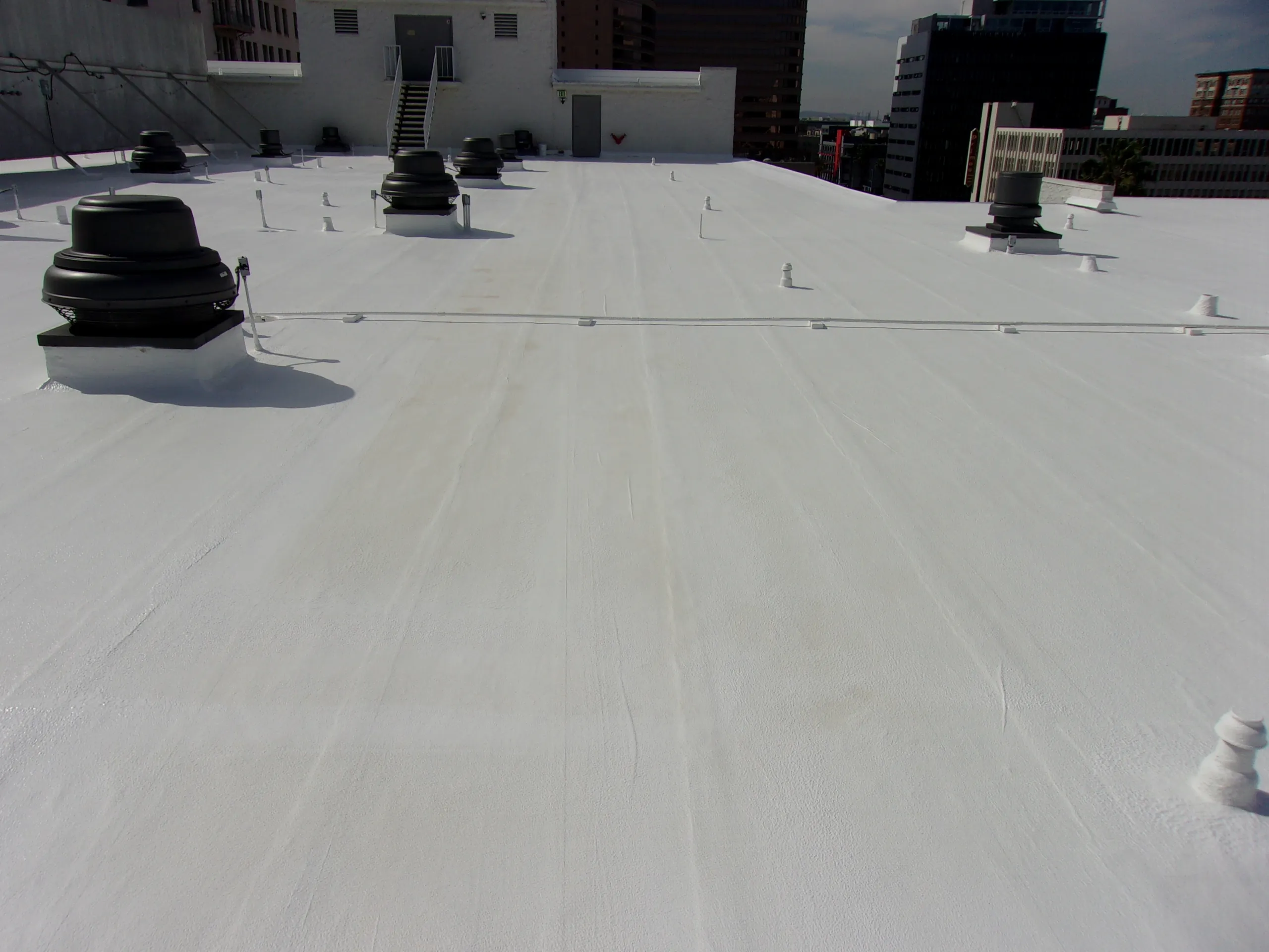 A flat commercial rooftop coated in white reflective material with several vents and access points visible under partly cloudy skies.